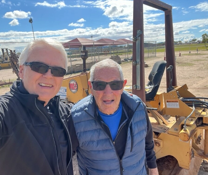 Two people standing next to a construction vehicle.