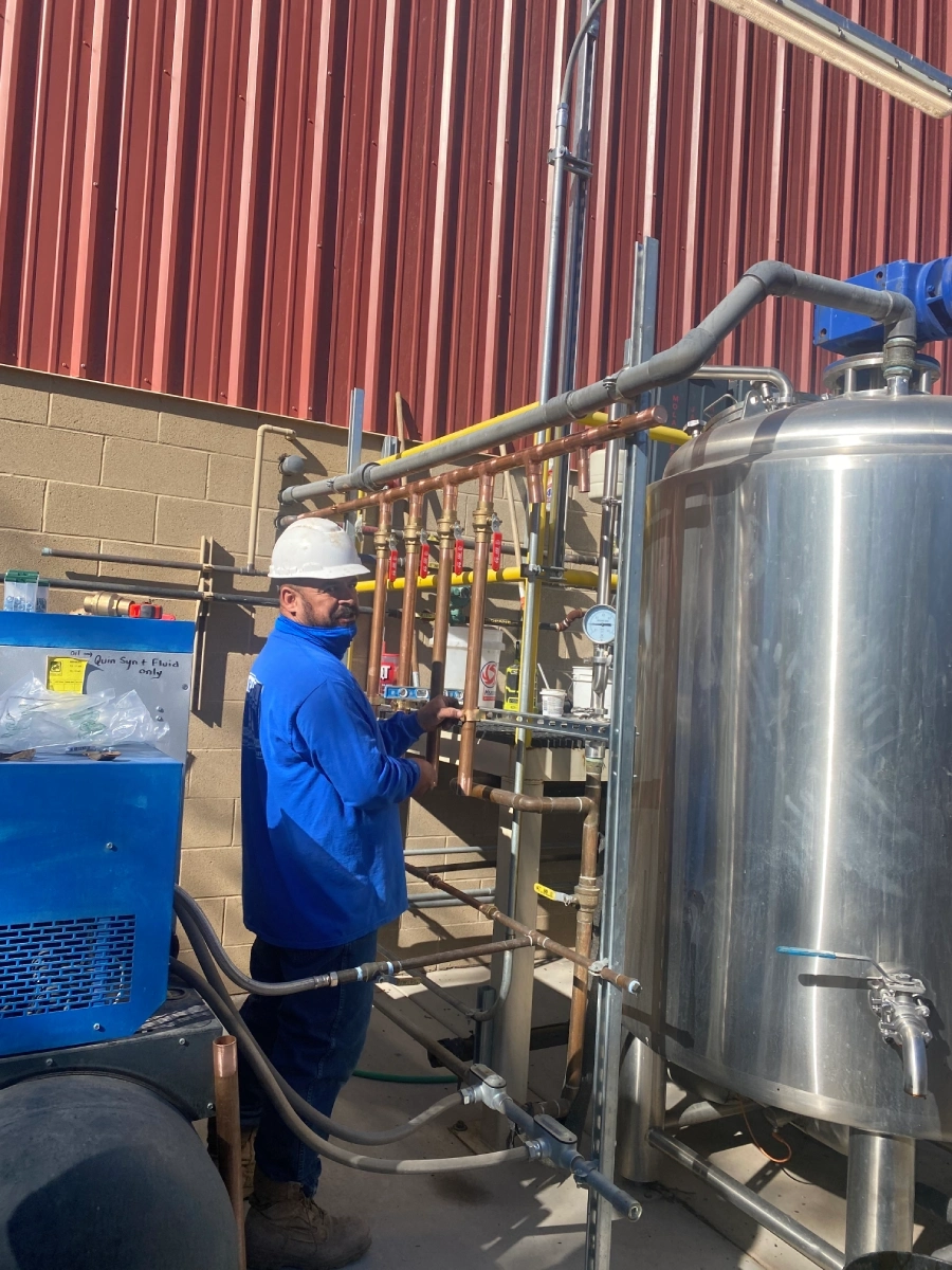 A man in blue jacket standing next to metal pipes.